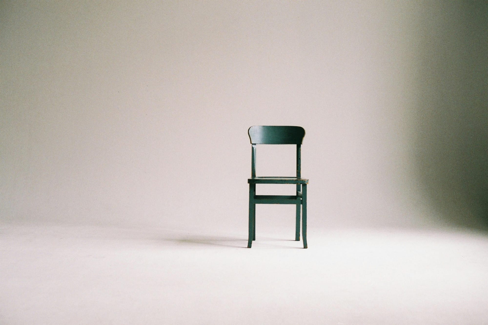 A simple black wood chair sits in an empty white room