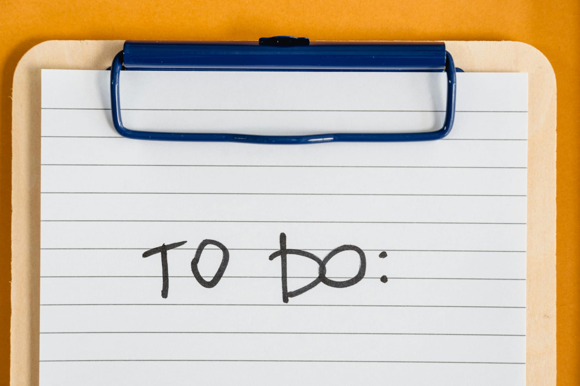 A clipboard has a single sheet of lined paper on it that reads "TO DO:" with an orange background