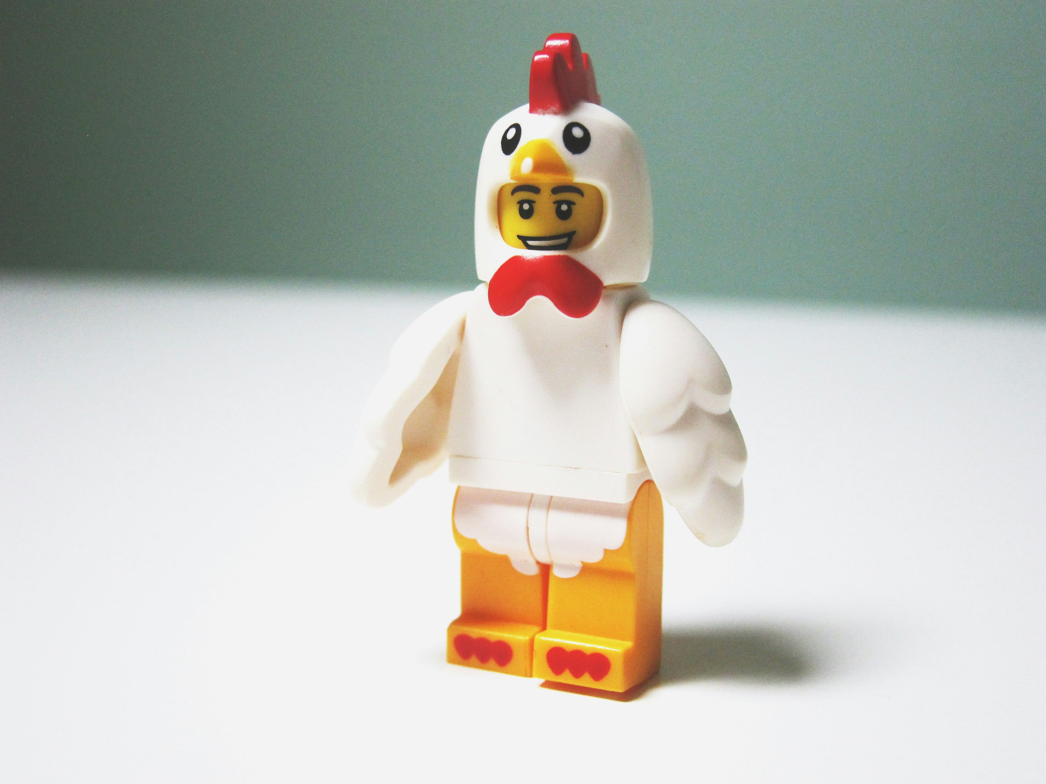 A smiling lego figure is wearing a chicken costume.